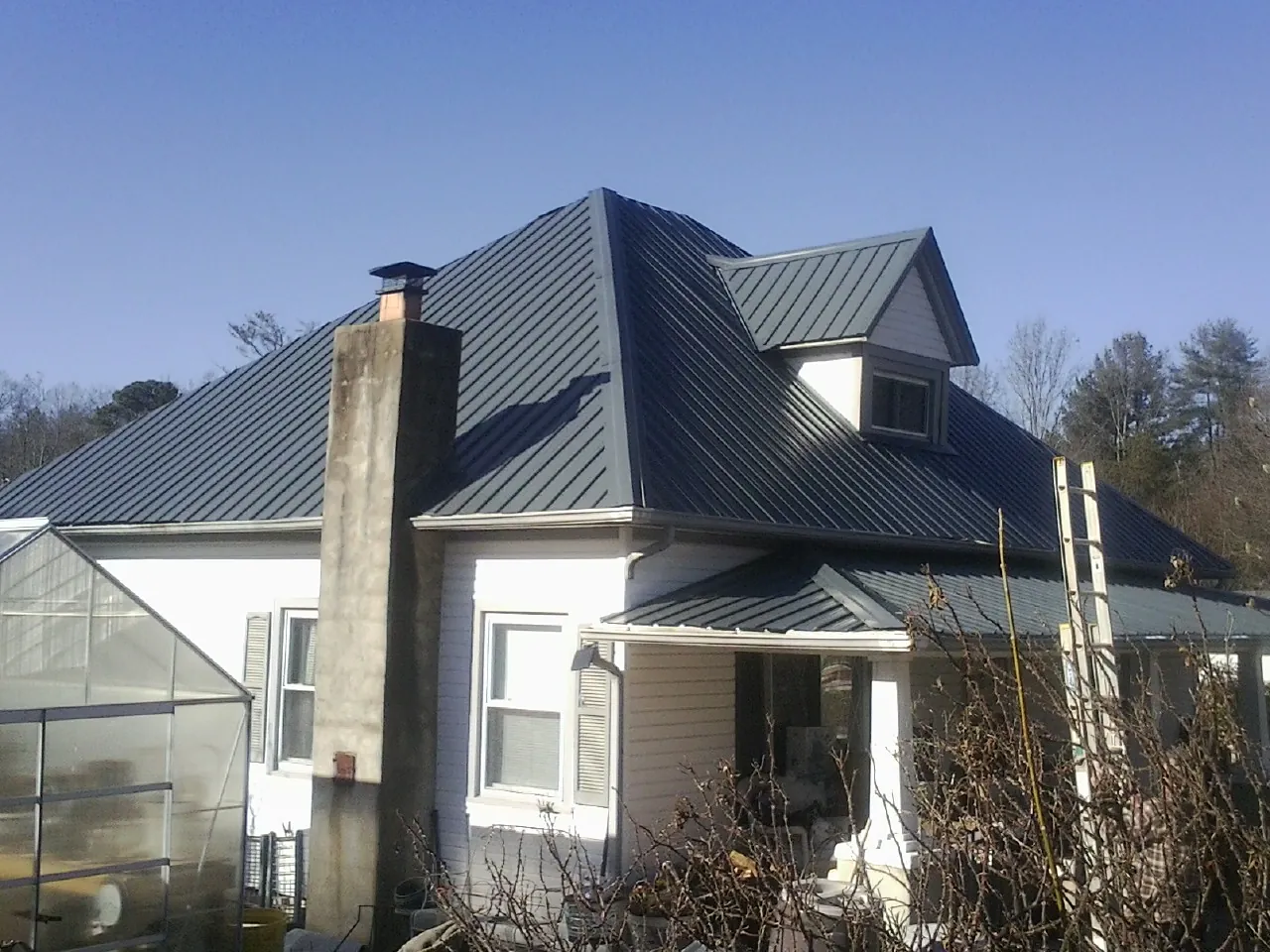 Dark blue standing seam metal roof on a white farmhouse with dormer — Slate & Tile Roof Repair by Roofing Brothers in Munday