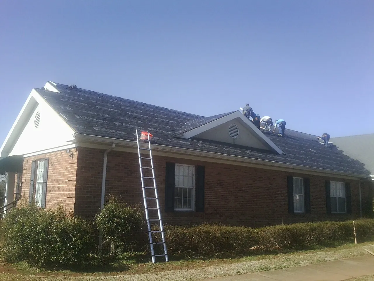 Crew tearing shingles off a brick ranch roof with a ladder set — Emergency Roof Repair work by our crew in Munday