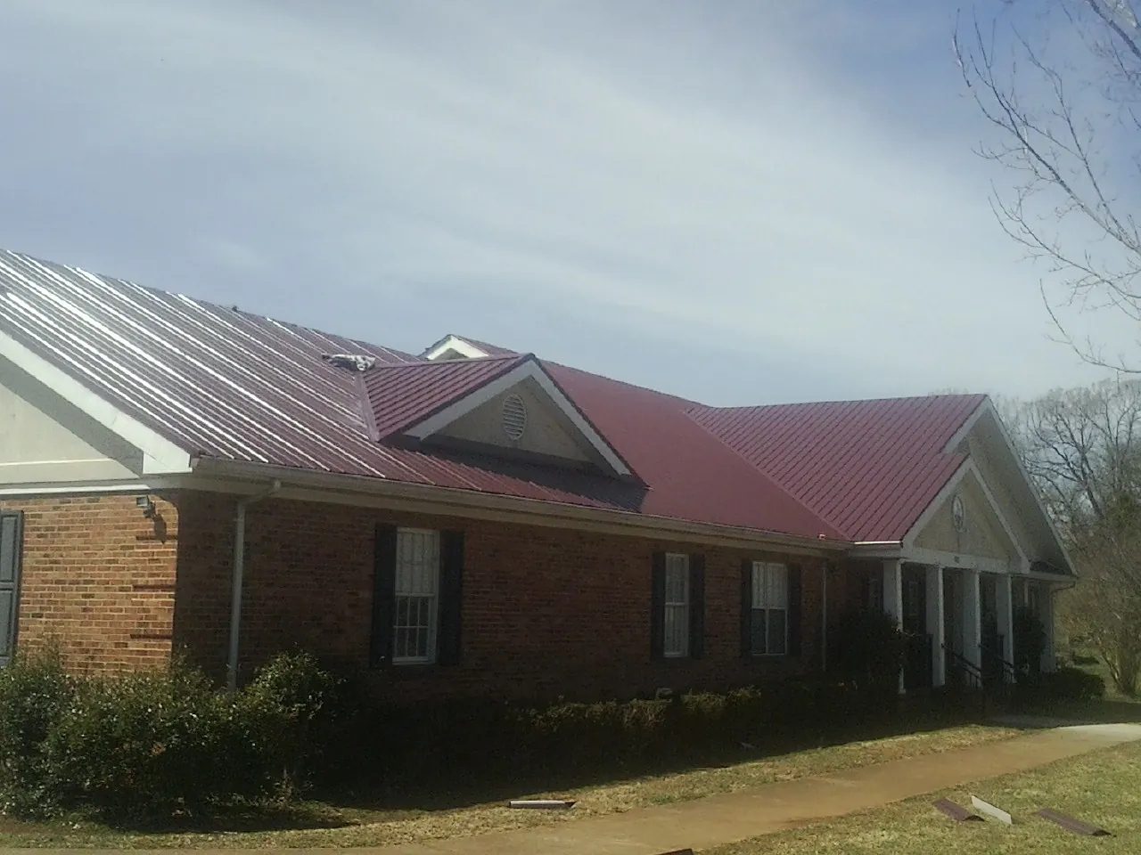 Red metal roof with gabled entries on a long brick building, from a Hail Damage Roof Repair job in Munday