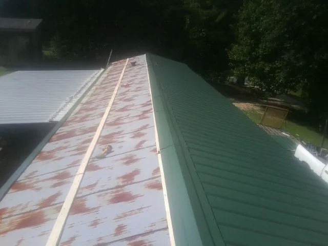 Old rusted panels beside newly installed green metal roofing — Wind Damage Roof Repair by Roofing Brothers in Munday