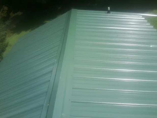 New green metal panels meeting at the ridge of a roof — Flat Roof Repair work by our crew in Munday