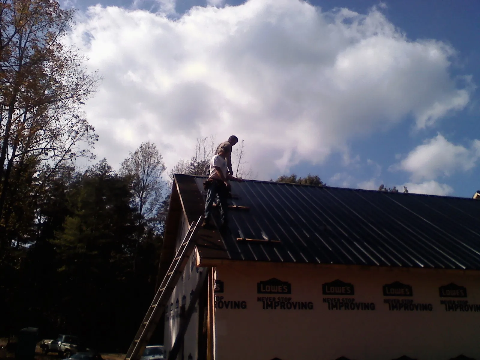 Roofer fastening dark metal panels high against a cloudy sky, from a Roof Inspection job in Munday