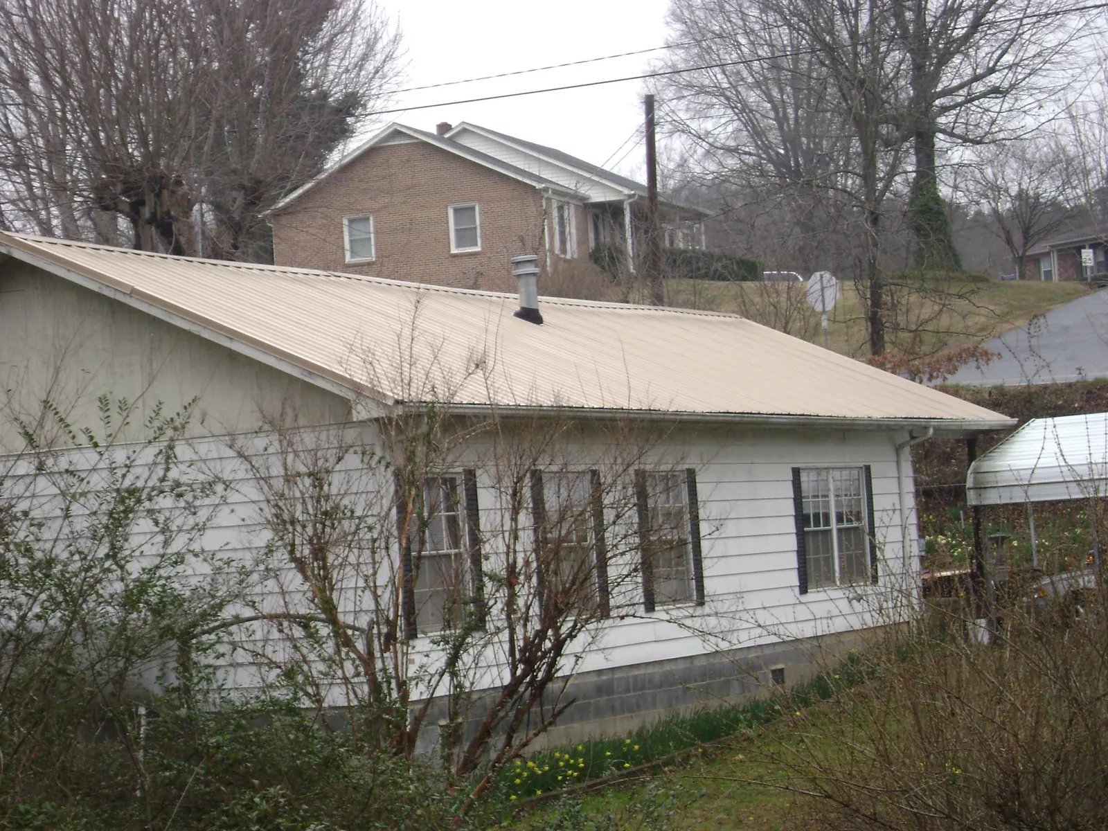 Tan metal roof on a white sided house set into a hillside — Commercial Roofing by Roofing Brothers in Munday
