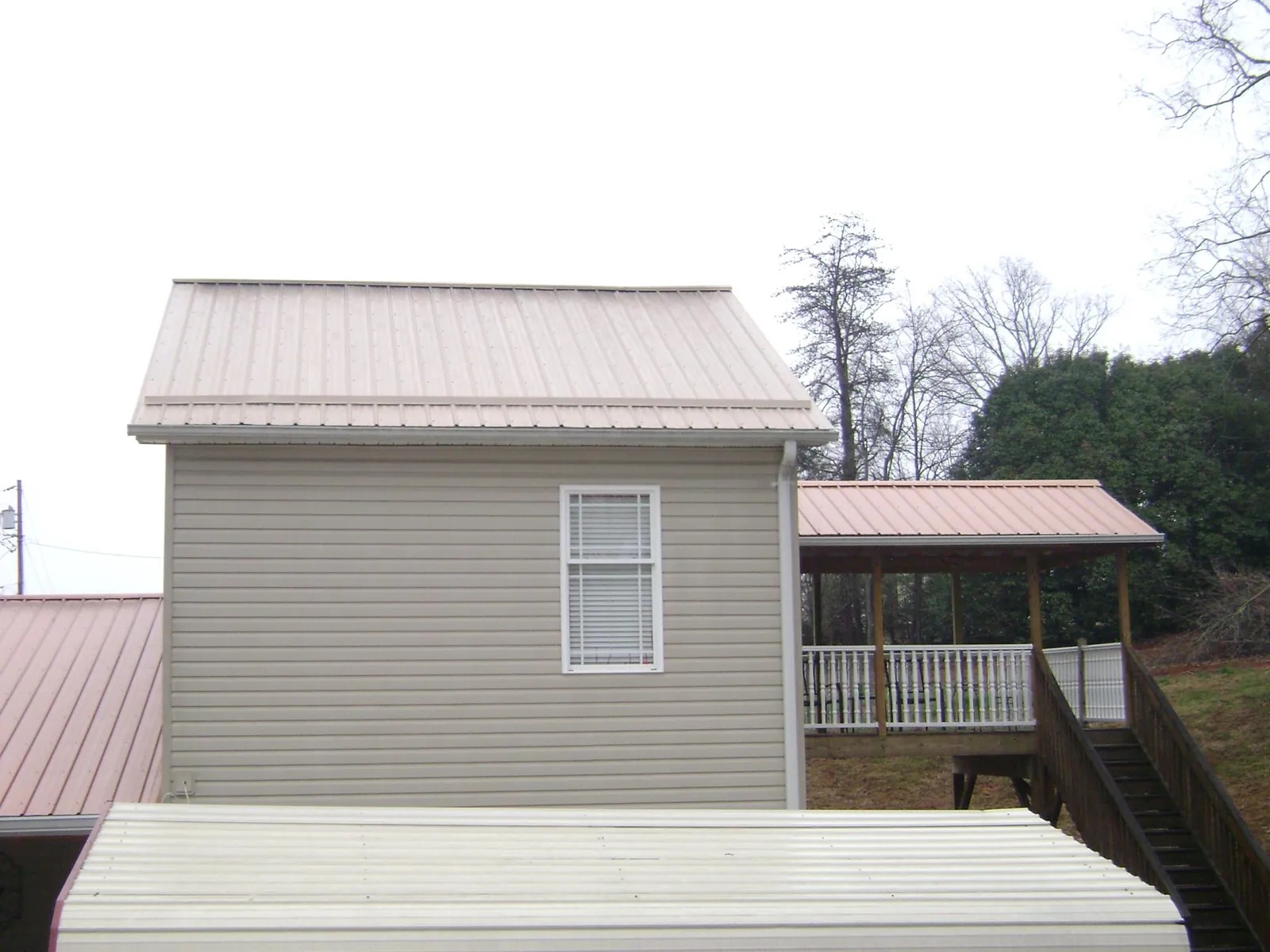 Tan metal roofs on a two story addition and attached porch, from a Roof Replacement job in Munday